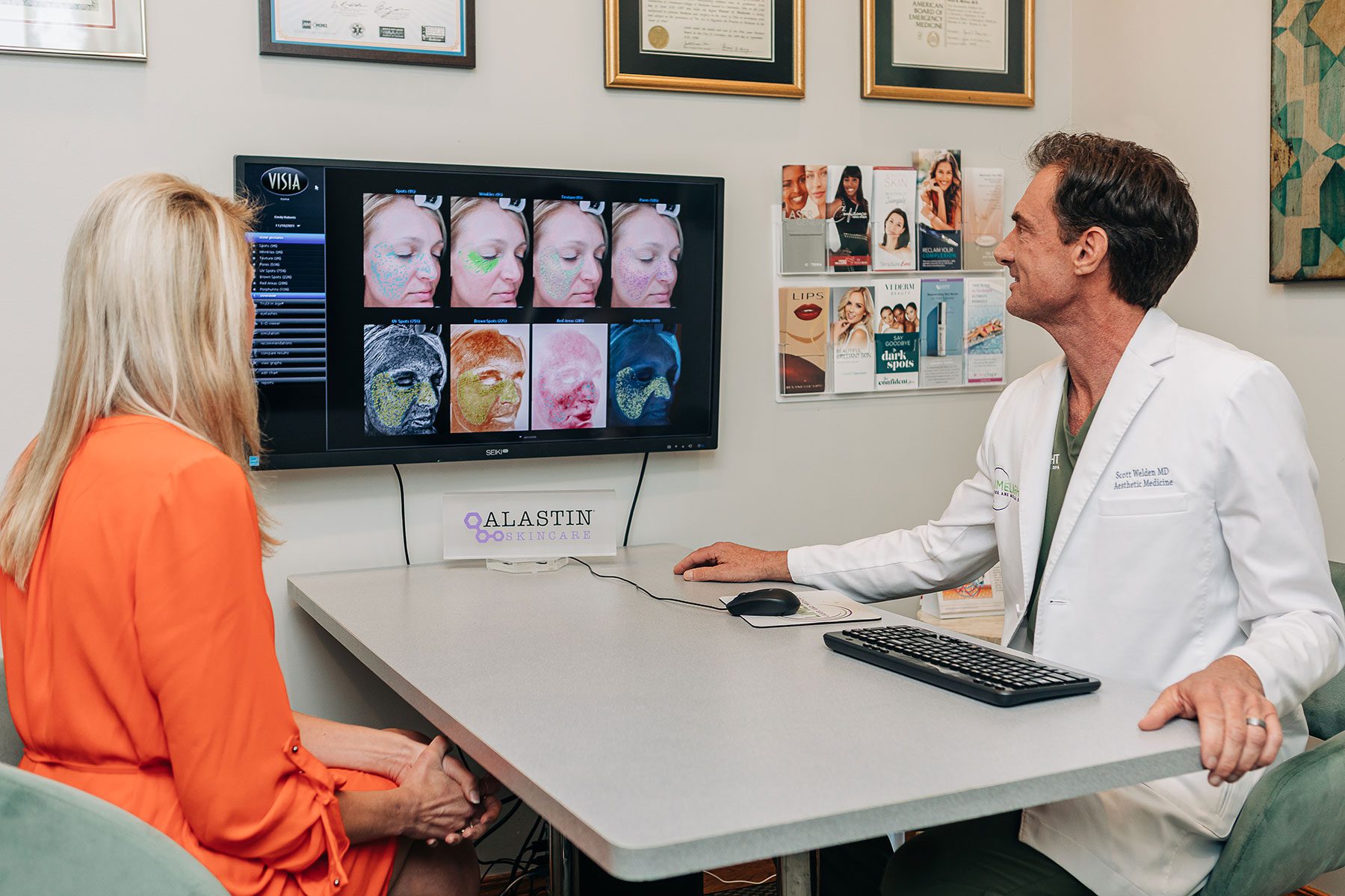 An experienced hair restoration surgeon from Wolf Hair Restoration Cincinnati shows a female patient skin analysis images on a computer monitor during a consultation in a medical office.