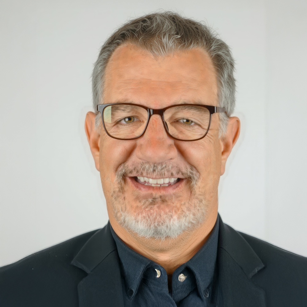 A middle-aged man with gray hair, glasses, and a salt-and-pepper beard smiles at the camera while wearing a dark blazer&mdash;exuding the confidence often seen in clients of experienced hair restoration surgeons in Cincinnati.