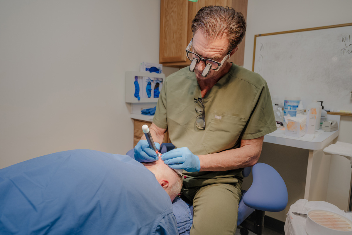 A man in a medical uniform performs an FUE hair transplant Cincinnati on another man's head, showcasing the precise technique used for natural-looking results.