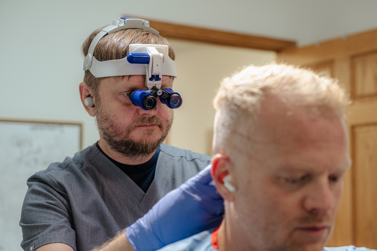 A medical professional wearing magnifying glasses examines the head of a patient in a clinical setting, preparing for an FUT Hair Transplant in Cincinnati.